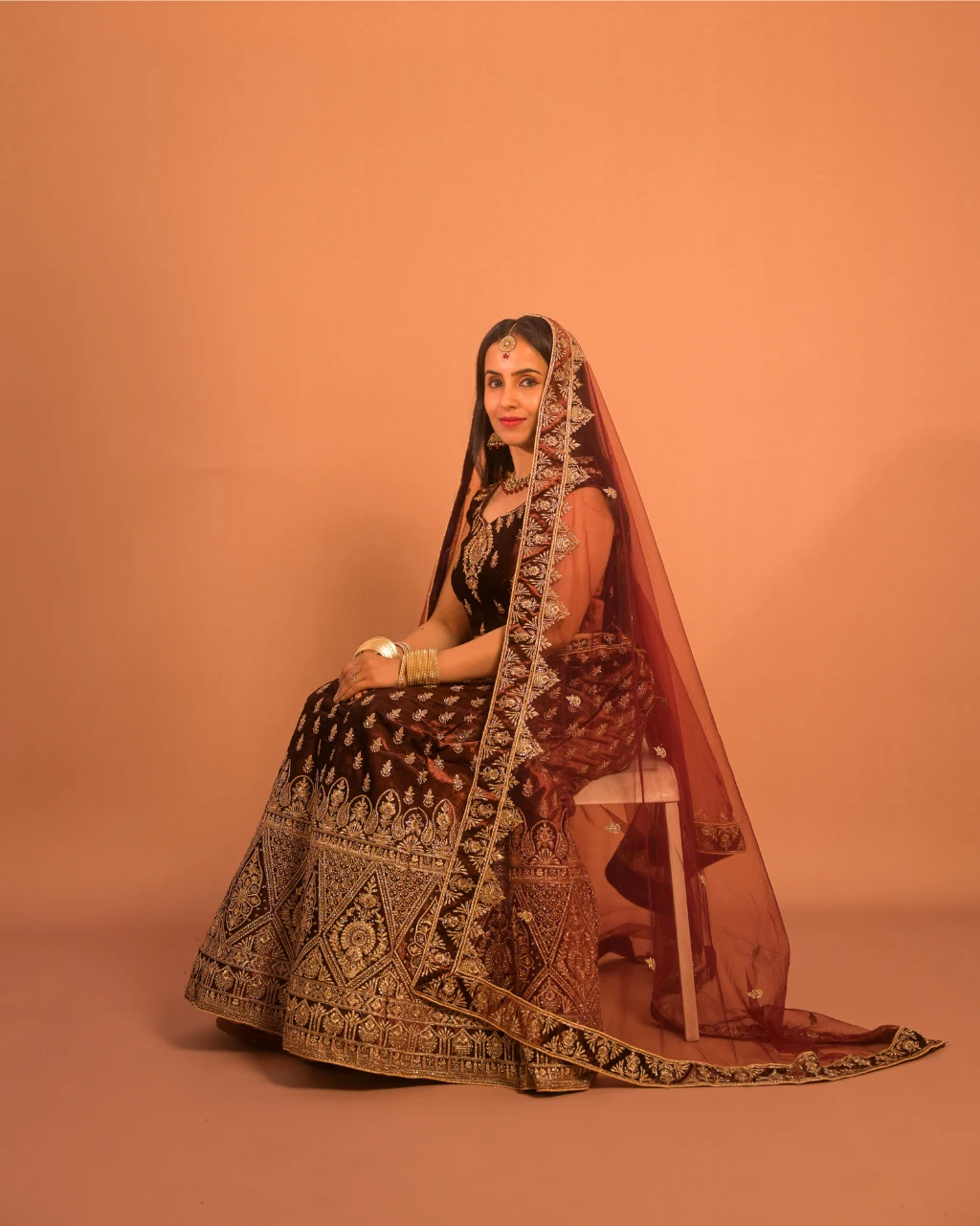 bride wearing brown and gold bridal lehenga seated studio photoshoot elegant look